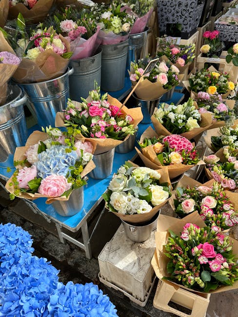 A variety of freshly cut floral arrangements displayed on a table at a flower shop, featuring bouquets with pink, white, and blue flowers including roses, hydrangeas, and chrysanthemums, wrapped in br